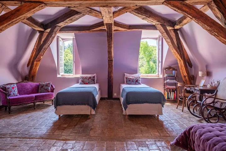Grande chambre sous charpente apparente, deux lits et fauteuils sous les fenêtres