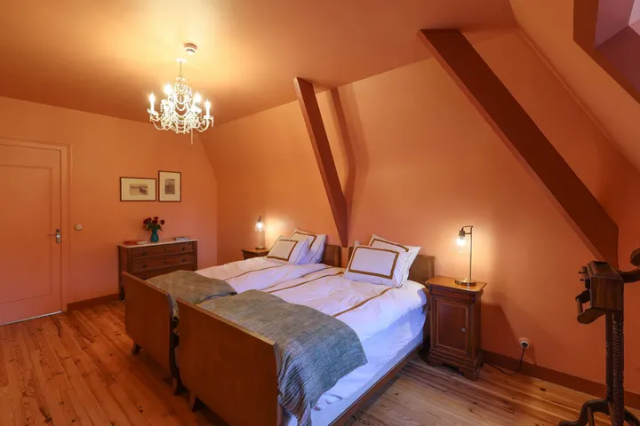 Chambre aux murs clairs sous poutres, lit double et lustre ancien