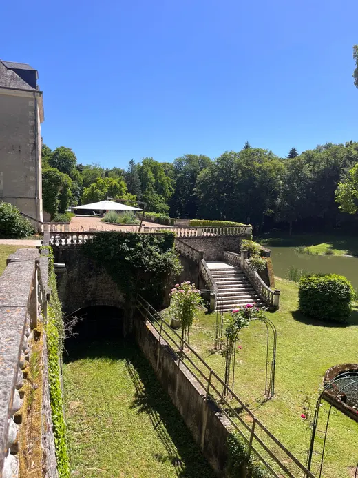Terrasse de pierre et pelouse descendant vers le parc, sous un ciel dégagé
