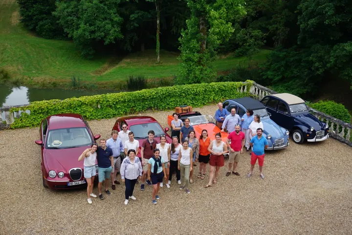 Un groupe d'une quinzaine de personnes réuni devant le château, voitures garées derrière