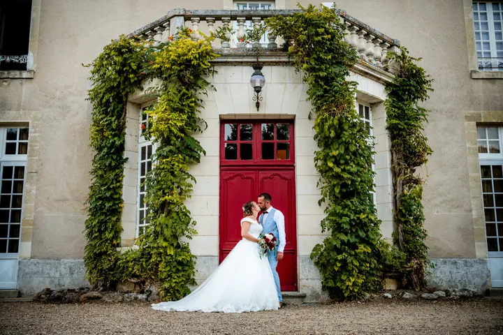 Les mariés devant la porte rouge du château, encadrée de vigne vierge