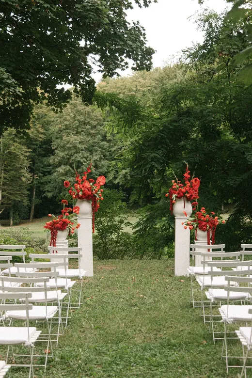 Allée de cérémonie dressée dans le parc, chaises alignées et colonnes fleuries