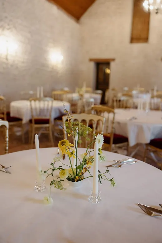 Salle de réception voûtée dressée pour un mariage, tables rondes nappées de blanc et chaises dorées à assise bordeaux