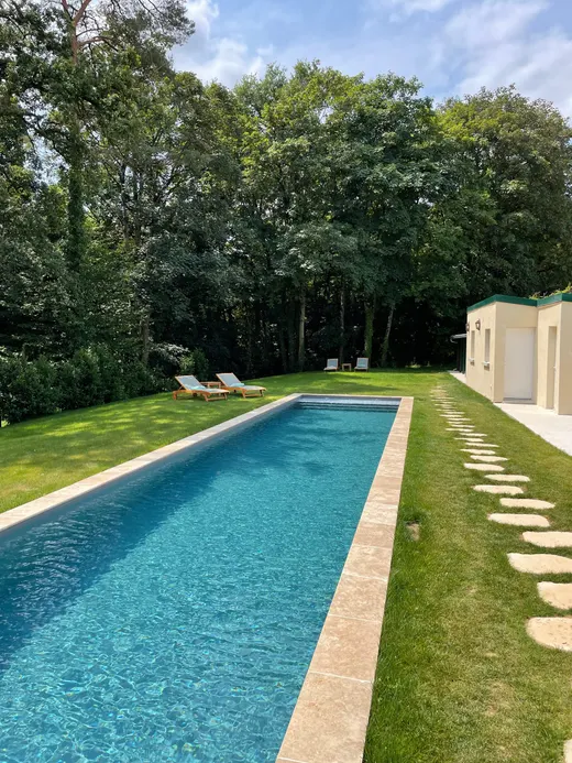 Le bassin allongé de la piscine chauffée, bordé d'arbres et de dalles de pierre