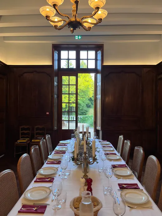 La grande table dressée dans la salle à manger boisée, chandeliers allumés et porte-fenêtre ouverte sur le parc