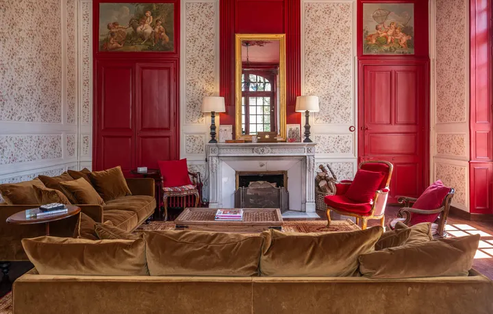 Le grand salon du château, murs rouges, canapés de velours et cheminée de pierre
