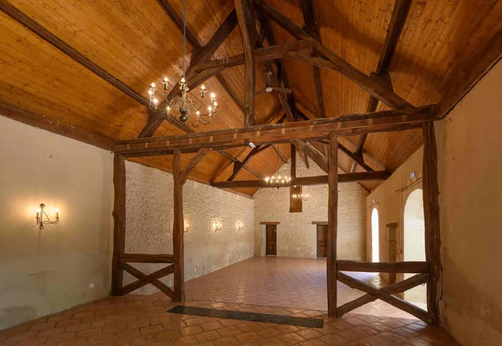 Grande salle vide sous charpente ancienne, sol de tomettes et lustres